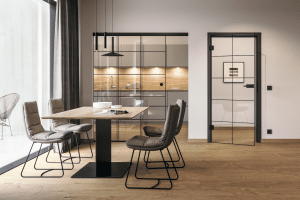 Hörmann Austria zeigt ein Esszimmer mit Holzboden und einer Essgruppe mit braunen Lederstühlen mit Zugang zur Küche durch eine Lofttüre mit schwarzem Rahmen.