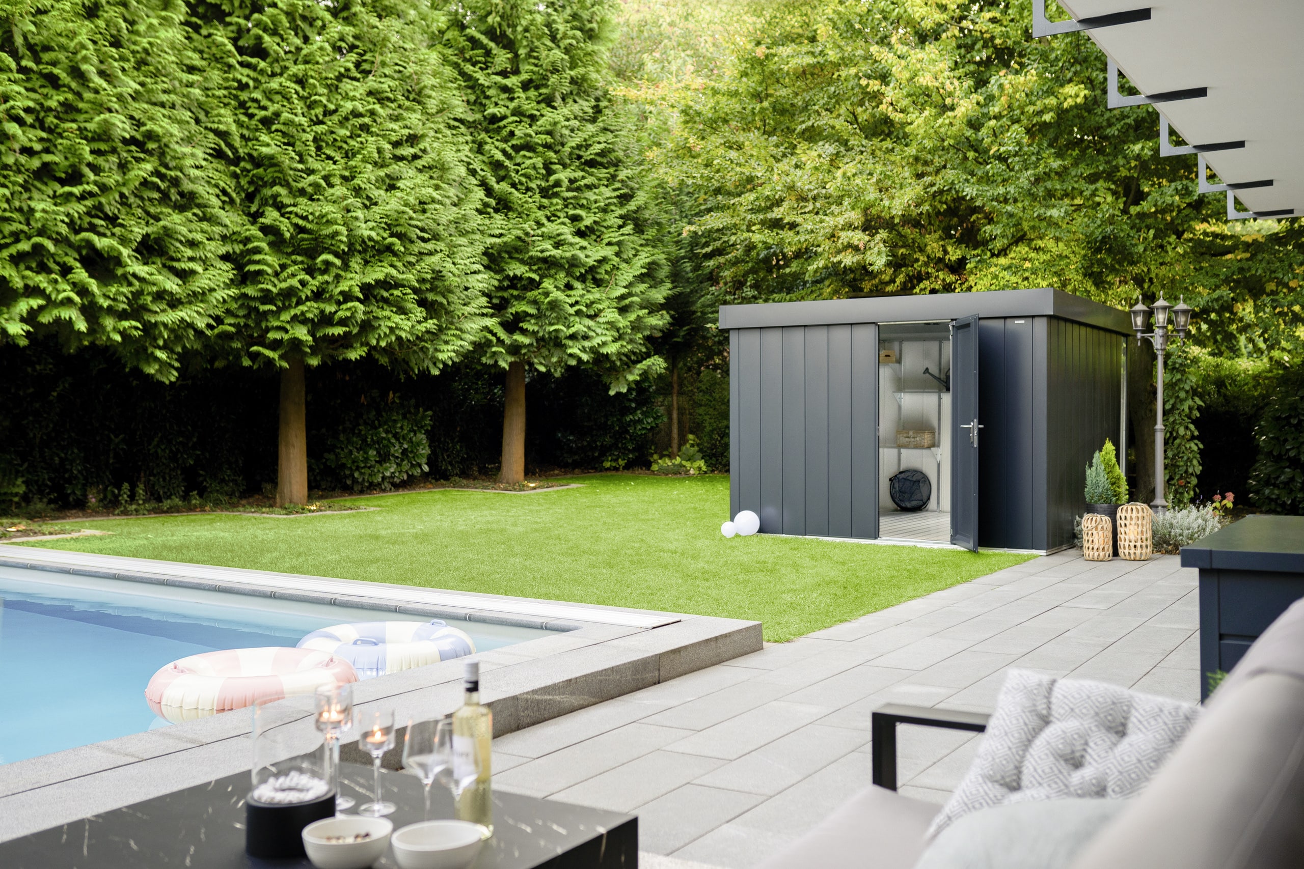 Modernes, geöffnetes Gerätehaus mit Flachdach in Anthrazit mit klarer, minimalistischer Gestaltung in einem Garten mit Pool von HÖRMANN AUSTRIA.
