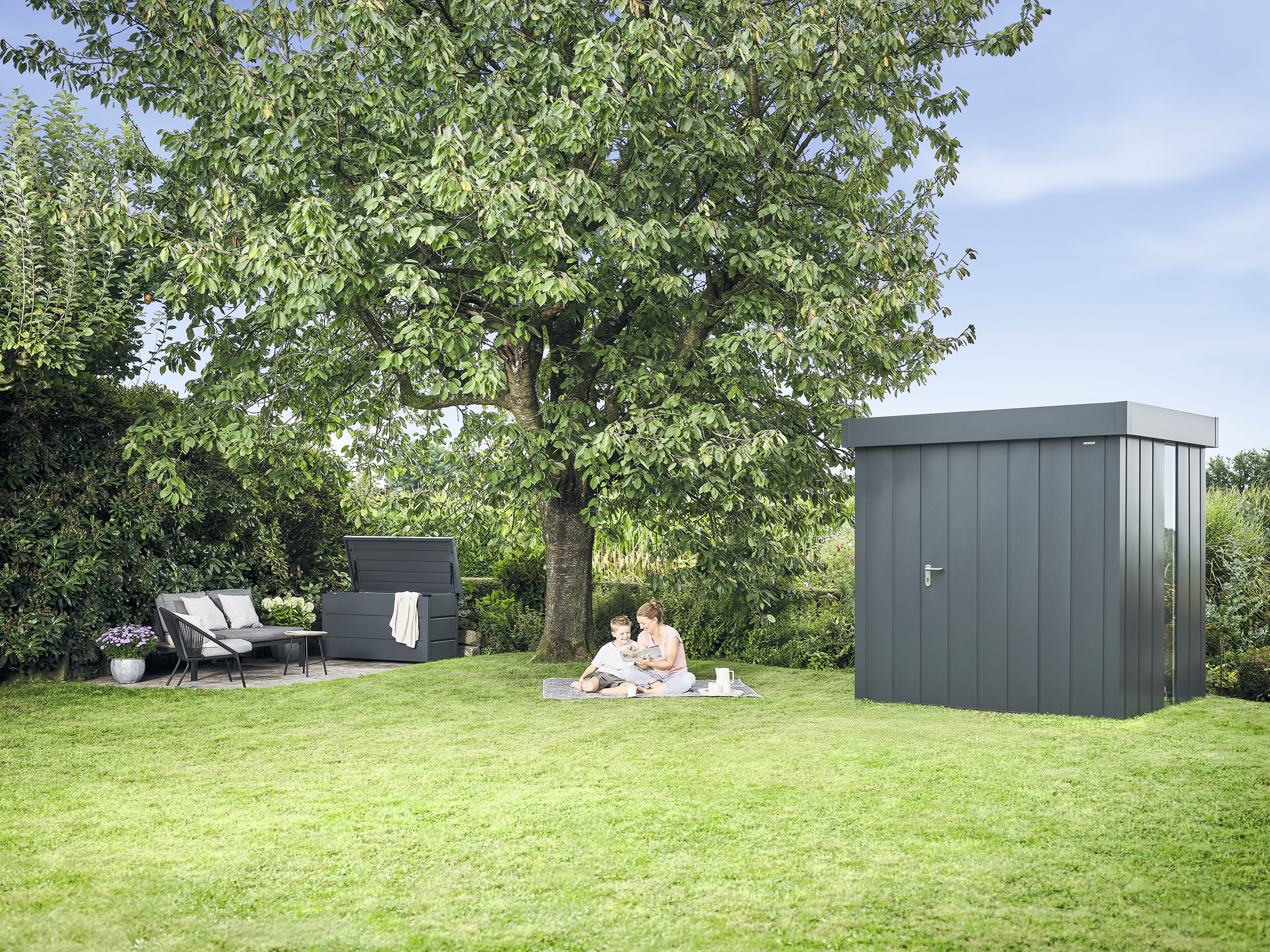 Obstgarten mit einer Juno Gartenbox und dem dazu passenden Gerätehaus mit Flachdach und bodentiefen Glaselementen in schwarzer Ausführung von HÖRMANN AUSTRIA.