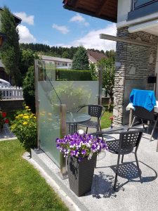 Terrasse eines Hauses mit einer freistehenden, satinierten Glasabzäunung welche als Wind- und Sichtschutz dient von Glaserei Hohl.