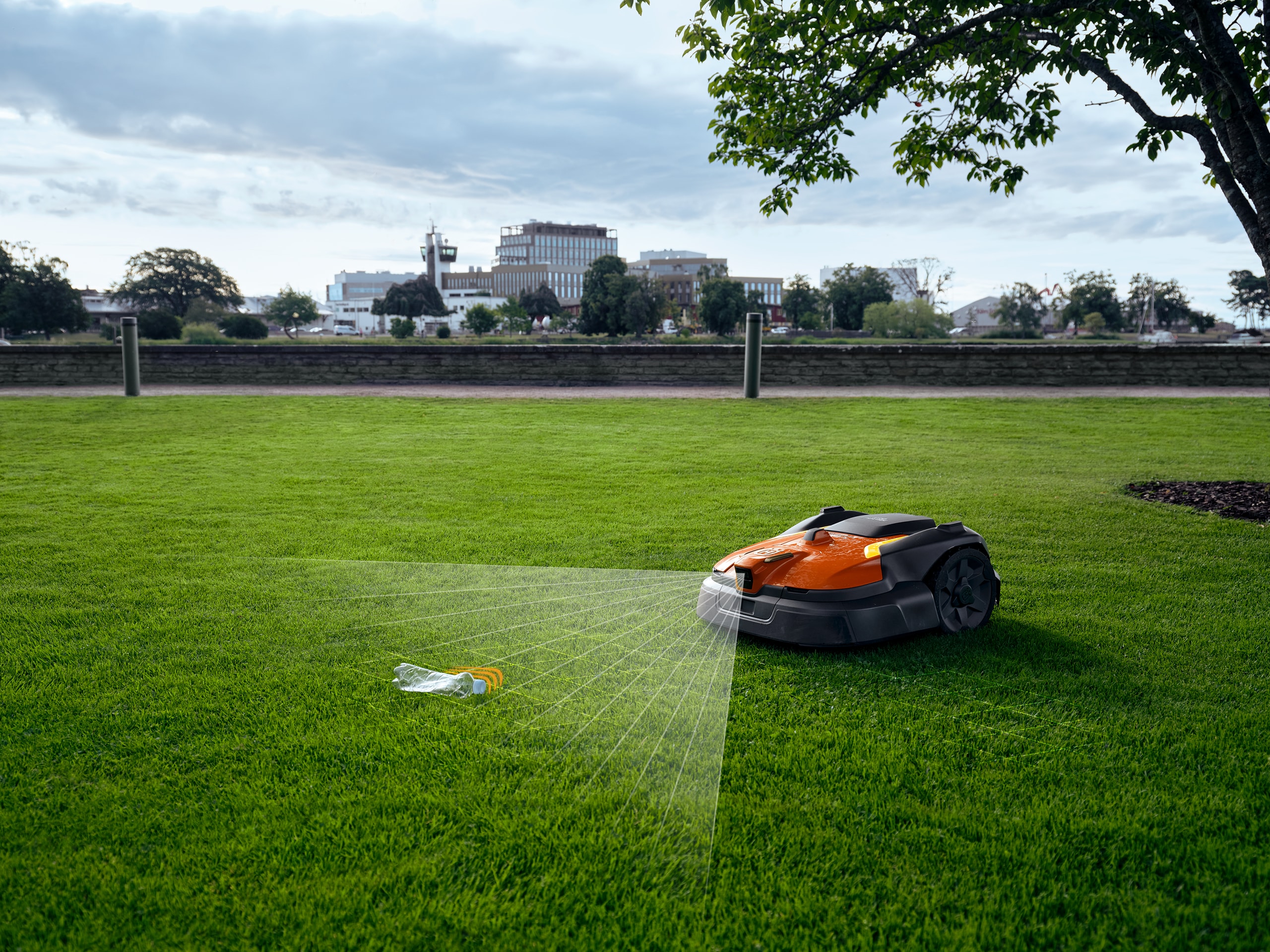 Husqvarna zeigt einen öffentlichen Park mit weitläufiger Rasenfläche, auf der eine Plastikfalsche liegt, die durch den Automower mittels Sensor als Hindernis erkannt wird.