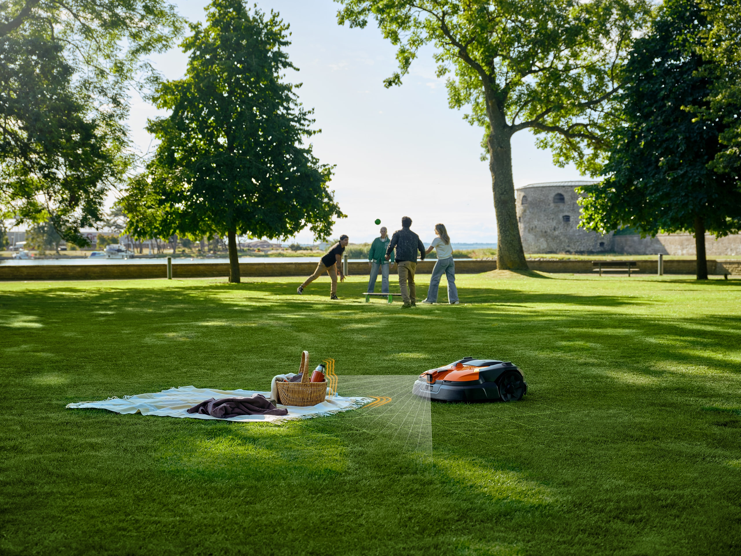 Husqvarna zeigt einen öffentlichen Park mit weitläufiger Rasenfläche, auf der eine Picknickdecke liegt, die durch den Automower mittels Sensor als Hindernis erkannt wird.