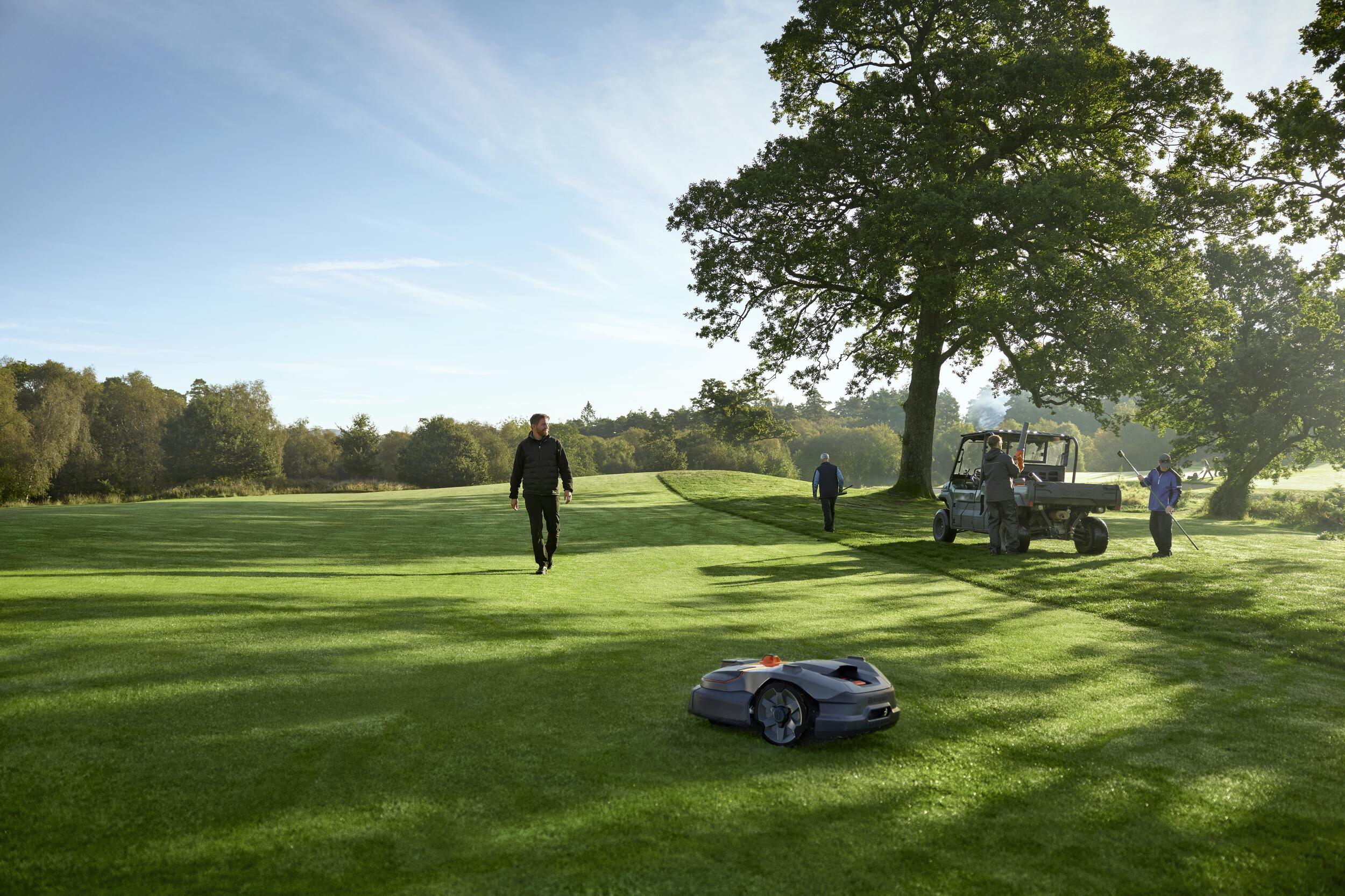 Husqvarna zeigt den Automower aus der 500er Serie auf einem Golfplatz mit weitläufiger Rasenfläche auf der sich einige Menschen bewegen.