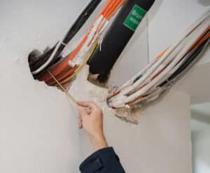 IBS Technisches Büro zeigt wie ein Techniker Leitungen, die aus einer Wandöffnung kommen, begutachtet und so die Qualitätssicherung des baulichen Brandschutzes durchführt.