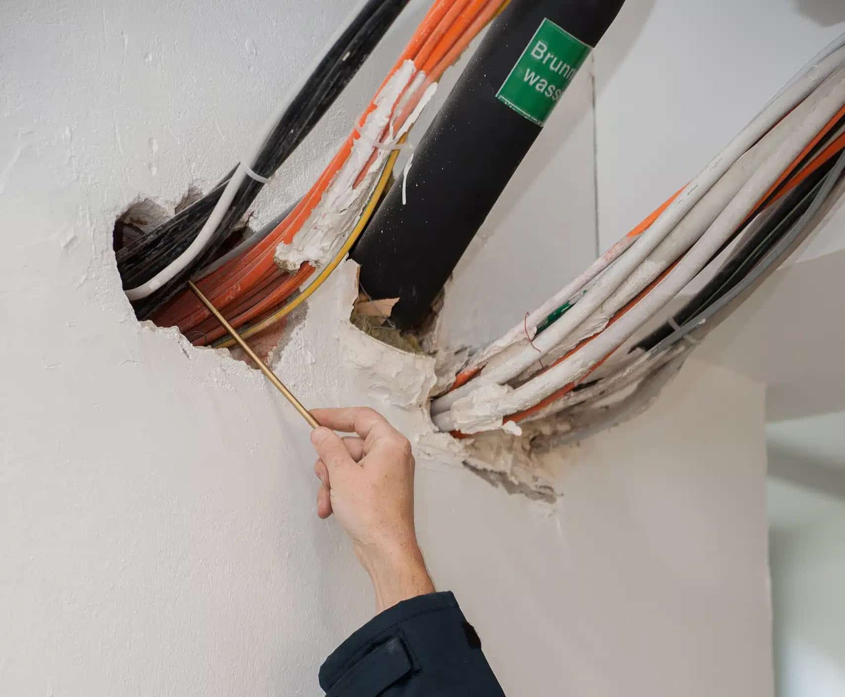 IBS Technisches Büro zeigt wie ein Techniker Leitungen, die aus einer Wandöffnung kommen, begutachtet und so die Qualitätssicherung des baulichen Brandschutzes durchführt.