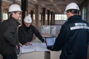 IBS Technisches Büro zeigt drei Techniker bei der Qualitätssicherung des baulichen Brandschutzes auf einer Baustelle.