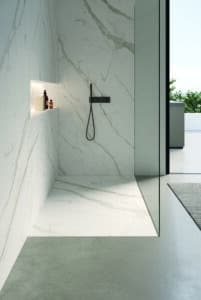 Barrierefreie Dusche mit Wandfliesen und Duschtasse in weisser Marmoroptik, gemauerter Ablage und mattschwarzer Armatur mit Stabbrause von Disenia.