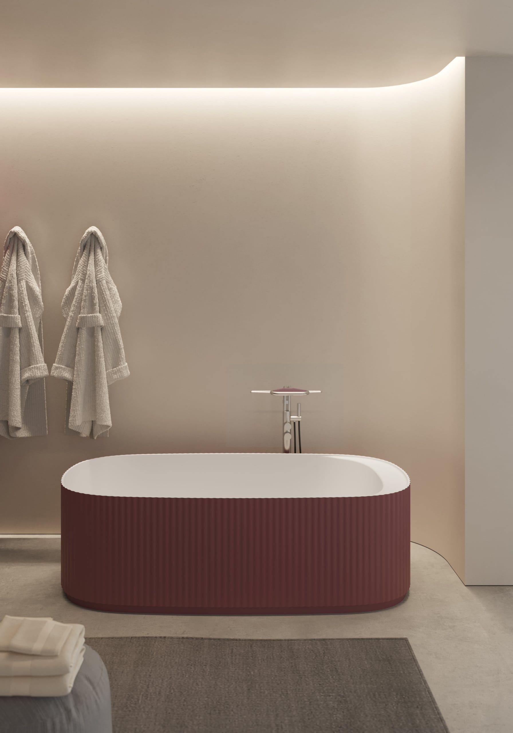 Freistehende ovale Badewanne mit geriffelter Bordeaux-Außenverkleidung, freistehender verchromter Armatur und Handbrause und roter Ablage vor einer indirekt beleuchteten, gewölbten Wand von Disenia.