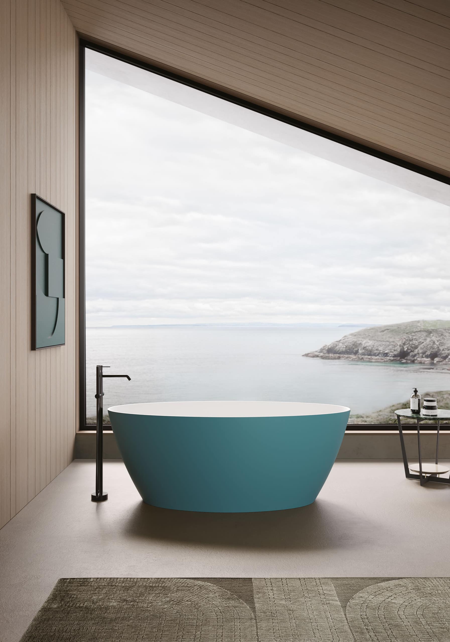Freistehende ovale Badewanne in dunklem Türkis mit freistehender sdunkler Armatur, platziert unter einer Dachschräge mit Panoramafenster und Blick aufs Meer von Disenia.