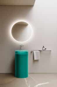 Freistehende zylindrische Waschsäule in halbtransparentem, satiniertem Türkisgrün mit Wandarmatur, rundem LED-Spiegel und silberner minimalistischer Utensilienleiste mit Ablage und Handtuchhalter von Disenia.