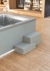 Der rechteckige Whirlpool "Helba 210" mit Ummantelung im grauen Betonlook, zwei Stufen, silbernem Innenleben und Touchscreen-Panel von Disenia.