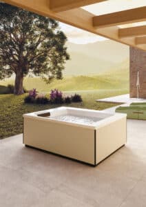 Terrasse mit XL-Steinfliesen, Pergola und Outdoor-Whirlpool "Linos" mit beiger Ummantelung mit schwarzem Sockel und Kantenprofilen und weissem Innenleben mit schwarzer Nackenstütze bzw. Einstiegshilfe oder Sitzfläche am Rand mit matter Oberfläche von Disenia.