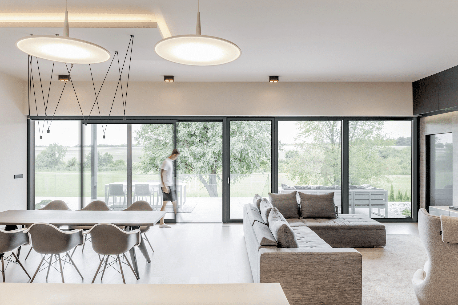 Internorm zeigt einen offenen Wohnbereich mit Couch und Essbereich und einer großen Fensterfront mit Glasschiebetür.