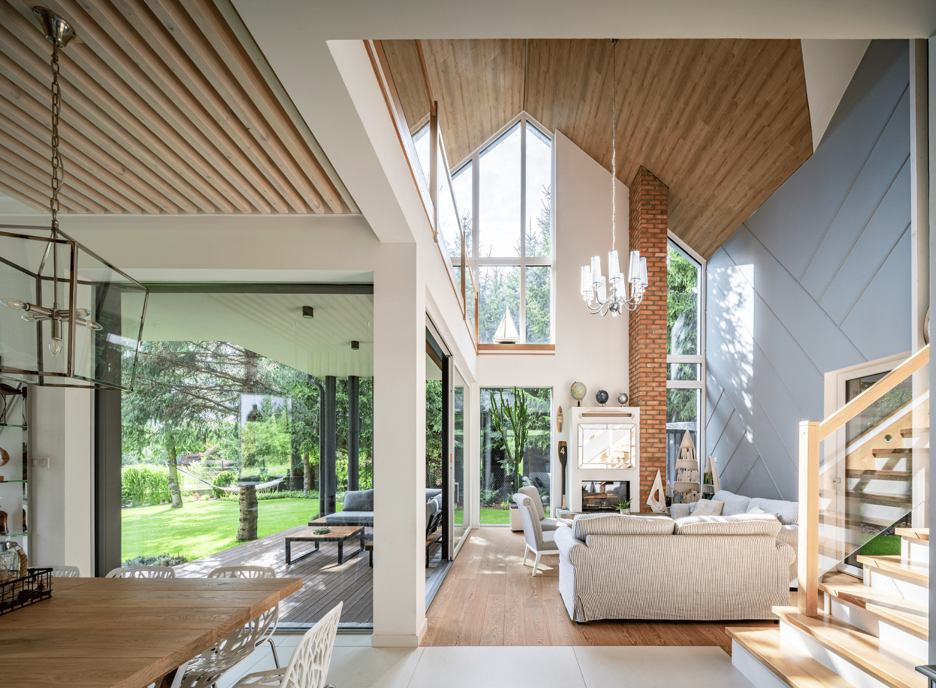Internorm zeigt den offenen Wohnbereich eines modernen Hauses mit hohem Dach und großen Fenstern, einer gemütlichen Sitzlandschaft und großzügigem Essbereich mit Hängelampe.