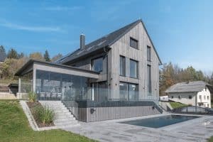 Internorm zeigt ein Einfamilienhaus mit Glasgeländer und großem Wintergarten mit Ganzglassystem.