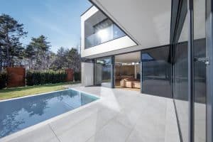 Internorm zeigt eine Villa mit Balkon und Glasgeländer und Ganzglassystem mit schwarzem Rahmen vor einer großen Terrasse mit Pool.