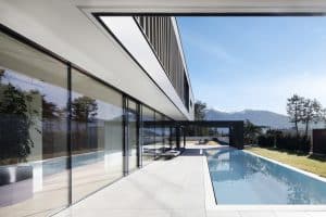 Internorm zeigt eine Hausfront mit Ganzglassystem mit schwarzem Rahmen vor einer großen Terrasse mit Pool.