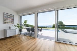 Internorm zeigt einen Wohnraum mit barrierefreiem Zugang zur Terrasse mit Pool über eine Glasschiebetür mit weißem Rahmen.
