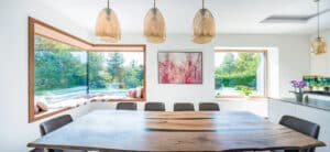 Ein Wohn- und Essbereich mit Küchenzeile samt Unterlichtfenster, Kochinsel, quadratischem Glaselement und einem Eck-Sitzfenster mit breitem Holzrahmen von Internorm.