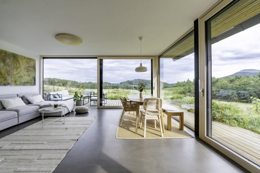 Ein Wohnzimmer mit großflächigen Terrassenschiebetüren und Eckverglasung mit Holz‑Alu‑Rahmen, innen in hellem Holz, außen in Schwarz von Internorm.