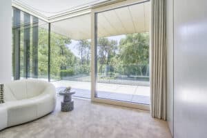 Modernes Haus mit Wohnzimmer, Teppichboden und Hebeschiebetüren und Eckverglasung zur Terrasse bzw. zum Balkon von Internorm.