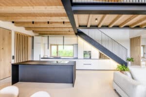 Haus mit offener moderner Wohnküche und Essbereich einer Treppe mit schwarzem Sprossengeländer, einem gut genutzten Untertreppenraum mit Küchenschränken und einer Holzdecke mit Balken von Internorm.