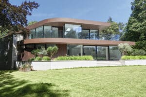 Eine Villa mit Fassadenmix aus Stein, viel Glas und kupferfarbenen Fassadenelementen im geschwungenem 1960er-Jahre-Stil mit Nurglasgeländer und Rundum-Balkon von Internorm.