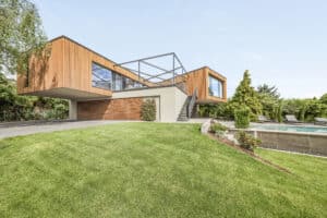 Eine moderne, verschachtelte Villa in einem Fassadenmix aus Holzfassadenelementen, Beton und Glas mit Garage, Pool und einer Dachterrasse mit Nurglasgeländer von Internorm.