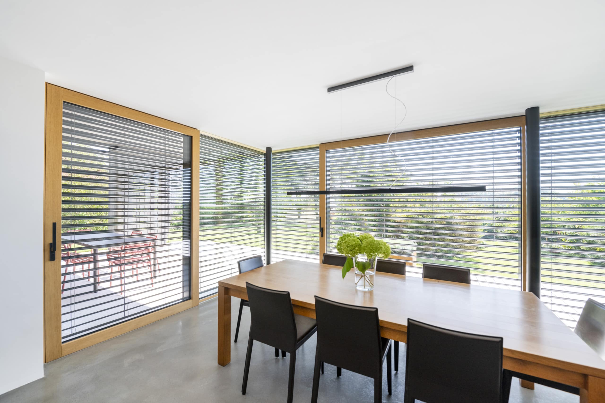 Ein moderner Essbereich mit Eckverglasung zum Terrassenbereich, großflächigen Terrassenschiebetüren mit Holzrahmen und Außenjalousien auf Halbmast von Internorm.