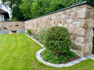 Großzügiger begrünter Garten mit Steinschlichtung und einer Feuerschale von JAHN Gewölbebau.