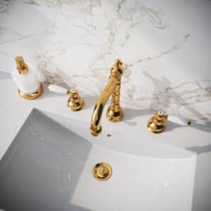 Ein Waschtisch mit 3‑Loch‑Batterie und Warm- und Kalt-Hebelgriffen mit weissem Porzellan in Gold und passendem Seifenspender von Jörger.