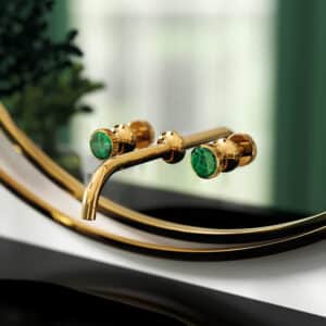 Ein am Wandspiegel montierte 3‑Loch‑Waschtischbatterie der Serie 'Valencia' in Gold mit grünem Malachit als Griffdetail von Jörger.