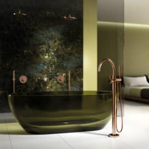 Eine freistehende grüngetönte Glasbadewanne mit Wannen-Einhandbatterie und Griffdetail in grünem Labradorit‑Naturstein von Jörger.