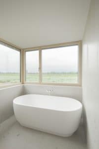 Helles Badezimmer mit freistehender Badewanne und großen Fenstern mit hellbraunem Rahmen von Josko.