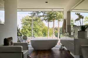 Ein modernes Badezimmer mit bodentiefer Fixverglasung zum Balkon mit Nurglasgeländer und einer freistehenden ovalen Badewanne von Josko.