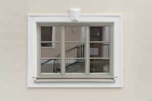 Aussenaufnahme eines Altbaus mit einem dreiflügeligem hellgrauen Kunststoff/Aluminium‑Sprossenfenster und klassischem Fassadenstuck von Josko.