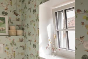 Ein Badezimmer im Altbau‑Stil mit weissen Kunststoff/Aluminium‑Sprossenfenstern mit goldfarbenem Drehgriff, verspielter Vogel-Tapete und romantischer Atmosphäre von Josko.