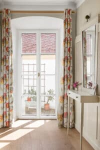 Ein romantisch gestalteter Wohnraum mit Gewölbe und Terrassentür mit weißen Kunststoff/Aluminium-Sprossen und goldfarbenem Griff, die den Blick auf die Terrasse öffnen von Josko.