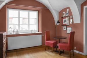 Ein (Küchen-)Stube mit Gewölbe und einem dreiflügeligen Sprossenfenster aus Kunststoff/Aluminium in Weiß, roten Wänden, Polsterstühlen, Stehlampe und Kaffeetisch von Josko.