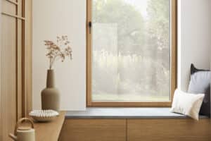 Ein kippbares Sitzfenster mit schwarzem Griff aus der Serie "Platin, 2. Generation" von Josko mit rahmenschlanker Holz‑Alu‑Konstruktion in Eiche in einem im Zwischen- bzw. Vorraum mit Garderobe.