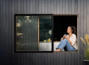 KDM Innovation zeigt eine Frau auf einem Sitzfenster, das Dank Movista Fensterbeschlägen per Schieben geöffnet werden kann.