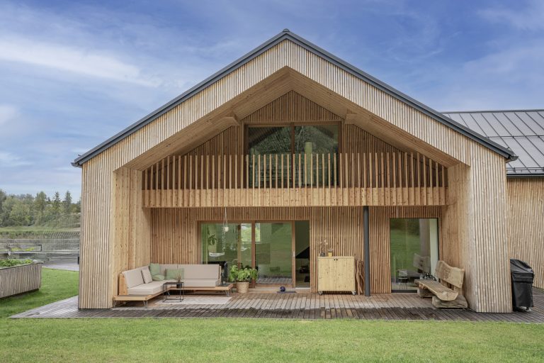 B. Kern Baugesellschaft zeigt Einfamilienhaus mit Holzfassade, Satteldach, Balkon und nach innenversetzter Terrasse.