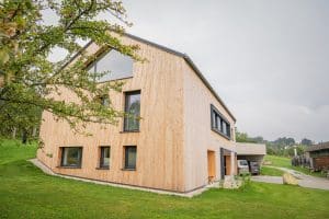 B. Kern Baugesellschaft zeigt Einfamilienhaus mit Holzfassade, Satteldach, Giebelfenster und Carport.