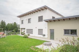 B. Kern Baugesellschaft zeigt Einfamilienhaus mit Pultdach, weißer Fassade, nach innen versetzter Terrasse und Garten.