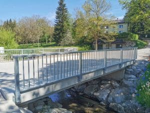 Eine über einen Fluß führende Betonbrücke mit beidseitigem Geländer aus verzinktem Stahl von Kickinger Bau.