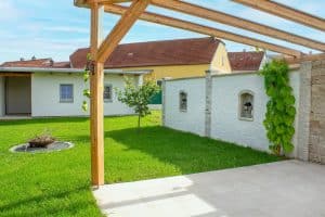 Gartenbereich mit Holzpergola, Steinmauer mit zwei Nischen mit Wandleuchten und Steinschlichtung von Kickinger Bau.