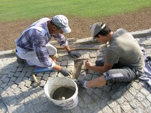 Zwei Arbeiter von Kickinger Bau bei der händischen Pflasterung eines Weges.