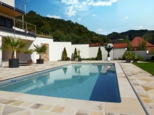 Eine mehrstöckige Villa mit großzügigem Terrassenbereich und einem Pool mit Steinumrandung und einem Fliesenboden mit Fliesen verschiedener Größen, angeordnet in einem Rautenmuster von Kickinger Bau.