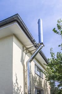 Edelstahl-Außenrohr eines Kamins montiert an einer Hausfassade mit Dachvorstand und Regenrinne von Kickinger Bau.