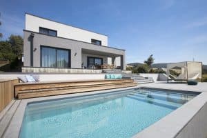 Flachdachvilla mit Dachterrasse, überdachter Terrasse mit Treppen zum Poolbereich mit einem Outdoor-Himmelbett und zweistufigem Sonnendeck aus Holz von Kickinger Bau.